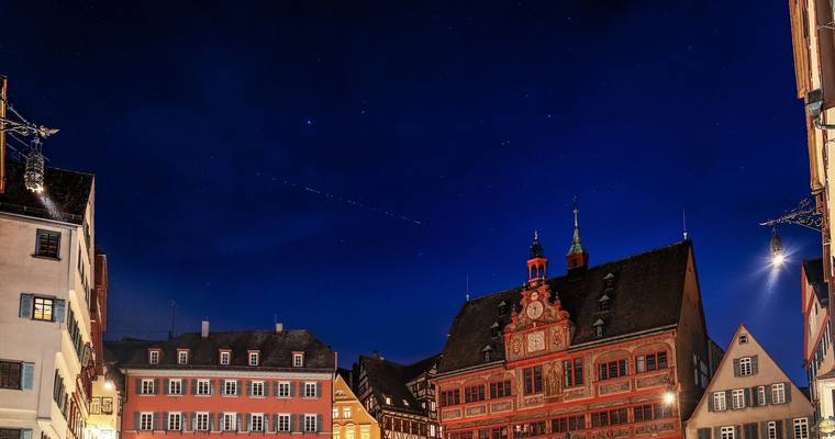 Nachthimmel über dem Tübinger Marktplatz mit Rathaus, darüber eine Kette von Starlink-Satelliten als Lichtpunkte