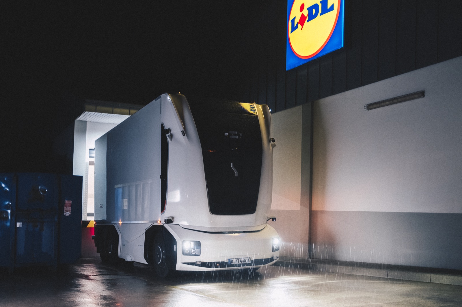 Weißer Elektro-Lastwagen ohne Fahrerhaus steht nachts im Regen an der Rampe einer Lidl-Filiale
